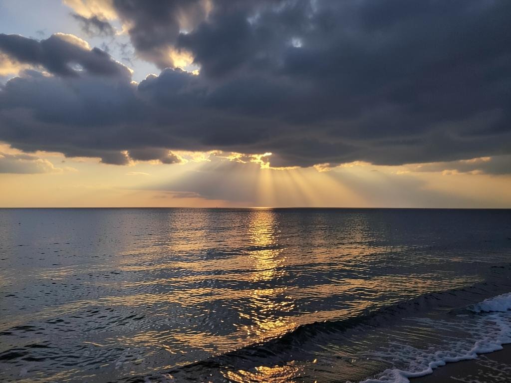 Mar calmo ao amanhecer com a luz atravessando as nuvens